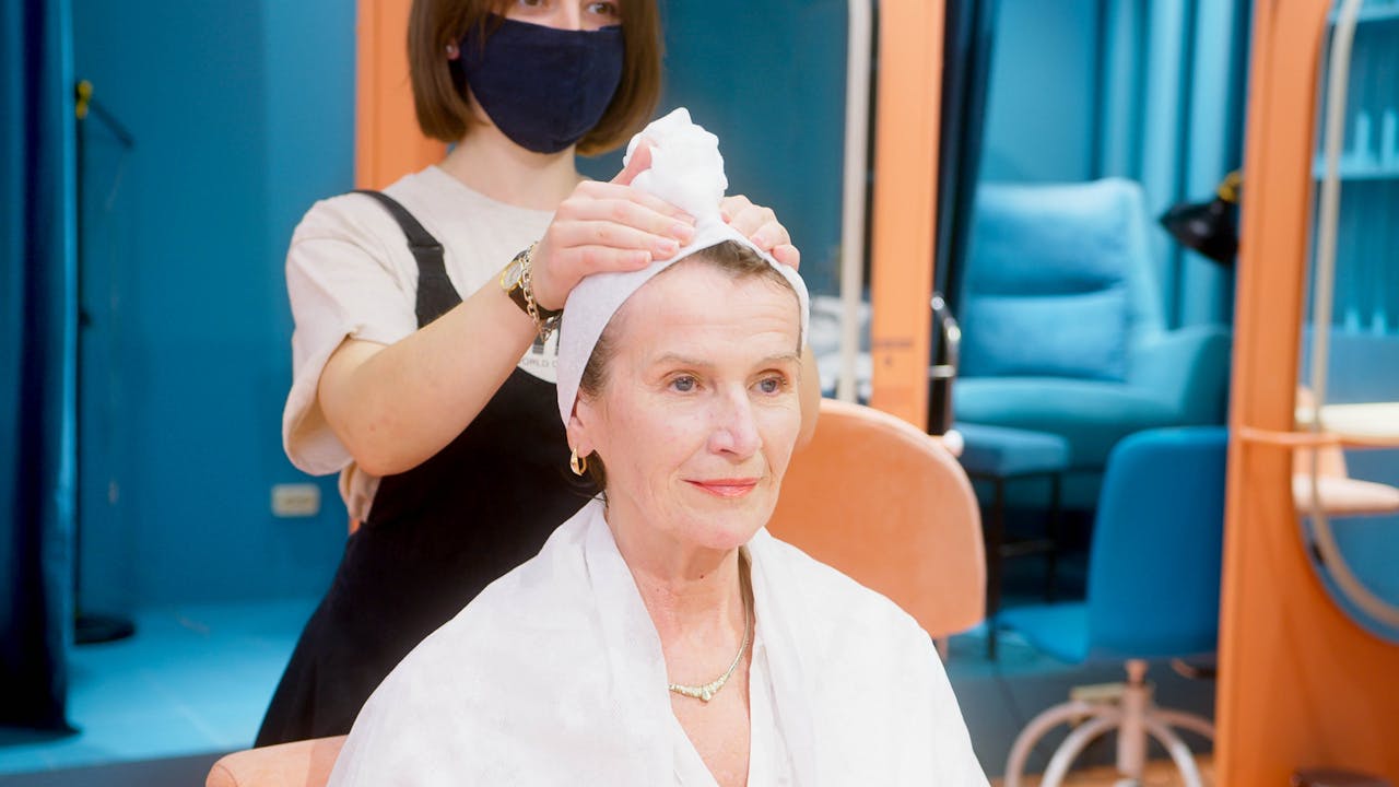 A senior woman is pampered with a hair treatment in a salon, highlighting the professional care provided.